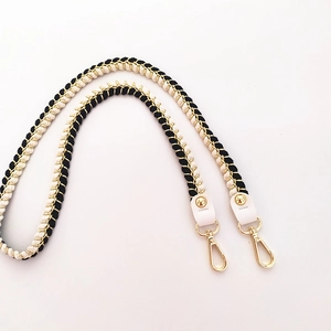 Detail of black and white woven shoulder strap with gold metal hooks and white leather ends