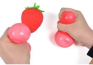 Detail showing hands squeezing a red strawberry squishy toy to reveal pink inner beads