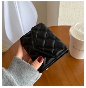 Close-up of a black quilted leather mini purse held against a clean desktop background