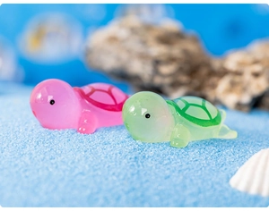 Close-up of small pink and green luminous resin turtles on blue miniature beach sand