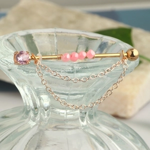 Detail view of golden industrial piercing with pink gemstones and hanging chains