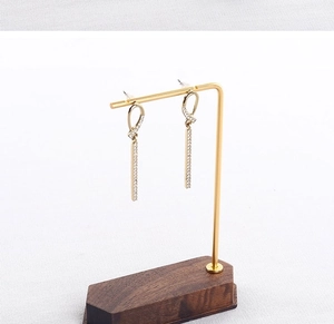 Detail of gold dangle earrings with sparkling zircons on a walnut and metal display stand