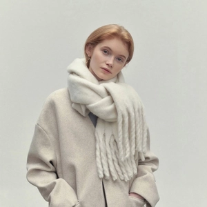 Detail of elegant cream-colored knitted scarf with fringe worn by a female model