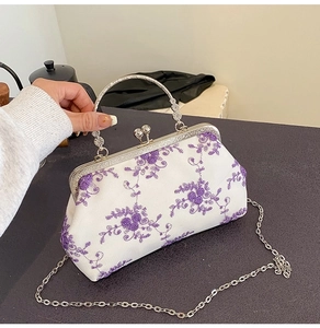 Macro view of vintage white fabric handbag with purple floral embroidery and metal handle