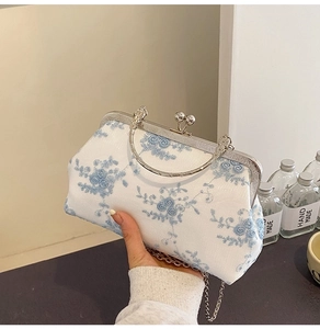 Detail of white lace clutch with blue floral embroidery and silver metal chain strap