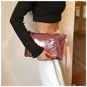 Detail of pink sequin mini clutch bag with gold zipper and wrist strap held by hand