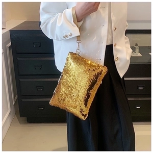 Detail shot of a mini golden sequin clutch bag with leather handle held by a model