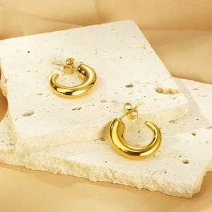Close-up of gold C-shaped stainless steel earrings on a beige stone base for a premium look