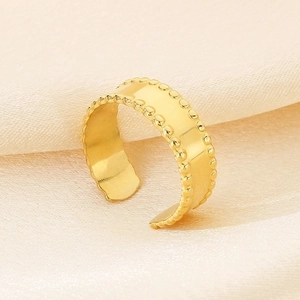 Detail of gold-plated textured wide open ring on a soft beige silk background