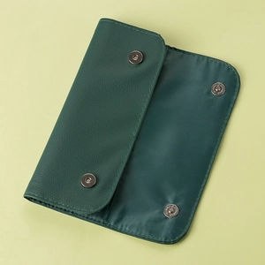 Detailed view of an open green faux leather makeup brush storage bag with metal snaps