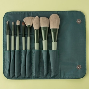 Detail of 8 makeup brushes stored in a dark green fabric roll case with metal snaps