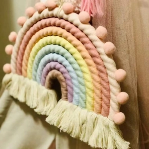 Detailed view of handmade woven rainbow wall hanging with pink pompoms and tassels