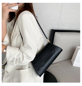 Detail of black crocodile texture leather shoulder bag against a white suit