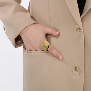 Close-up of a large gold oval stainless steel ring worn by a model in a beige suit