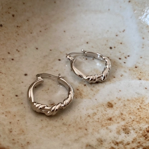 Macro detail of minimalist S925 sterling silver knotted hoop earrings on ceramic