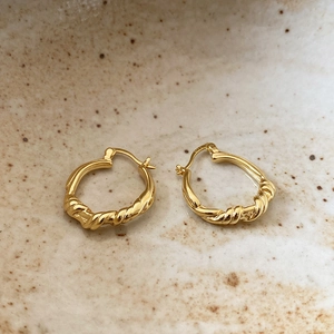 Macro shot of S925 sterling silver gold-plated twisted knot earrings on ceramic