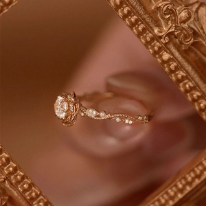Golden rose-shaped ring with round brilliant zircon and twisted vine band inside a frame
