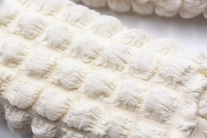 Macro shot of the soft popcorn textured fabric on the cream-colored puff makeup bag