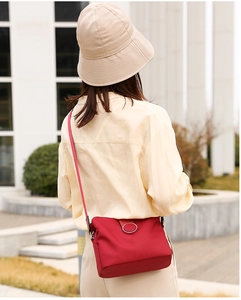 Outdoor shot of a red nylon crossbody bag with silver ring clasp on a yellow shirt