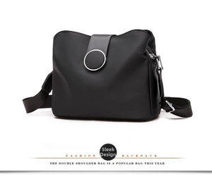 Detail view of the black nylon bag featuring a round buckle and silver metal zipper