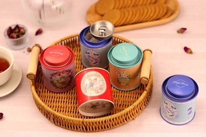 Detail view of round tin tea canisters with vintage rabbit illustrations on a wicker tray