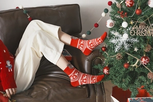 Woman wearing red Christmas socks with reindeer patterns on a sofa by a festive tree