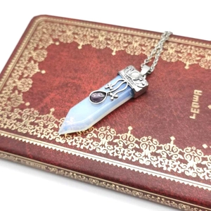 Close-up of hexagonal opal pendant with purple crystal on vintage floral book cover