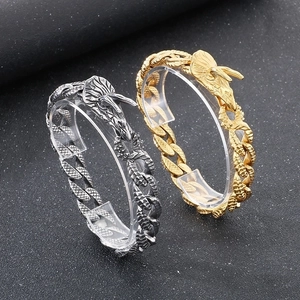 Detailed close-up of gold and silver dragon head cuban link bracelets on black display