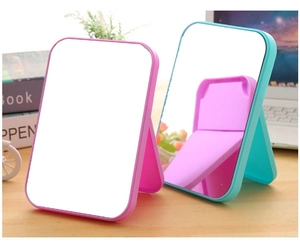Close-up of portable pink and blue folding makeup mirrors on a wooden desk setup
