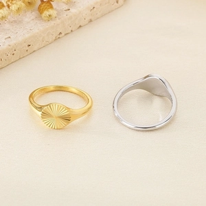 Detail of gold and silver sunflower signet rings on a textured stone and fabric background