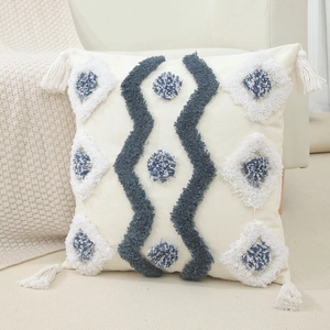 Bohemian tufted pillow cover in cream with blue fringe tassels on a cozy beige sofa