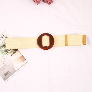 Detail of beige woven straw belt featuring a large round wooden buckle and natural texture