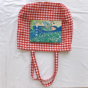 Close-up of a red and white gingham canvas tote bag with matching straps on a white fabric