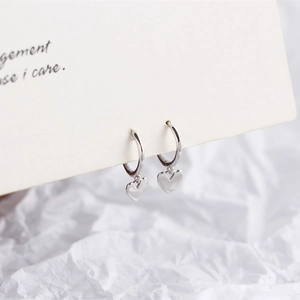 Detail shot of small silver heart charms on hoop earrings held on a paper card
