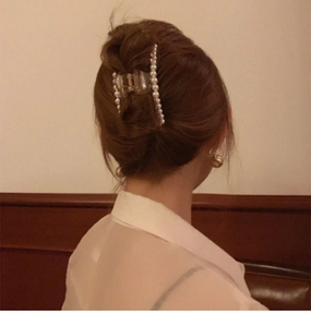 Detail of a pearl hair claw clip securing a brown hair bun in warm ambient lighting
