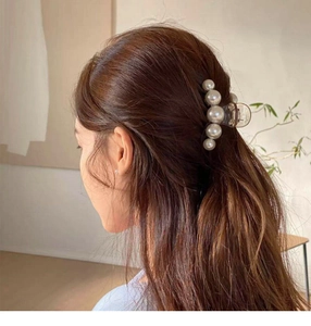 Close-up of a clear hair claw clip featuring elegant white pearls worn on dark hair