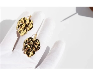 Detail view of large gold monstera leaf earrings held in a hand for size scale