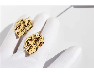 Macro detail of gold plated leaf earrings with artistic hammered metal texture