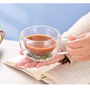 Detail of hand holding a double-walled glass cup with liquid and dried flowers