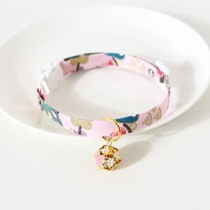 Close-up of pink floral fabric pet collar with a golden cherry blossom bell in a white dish