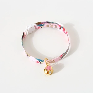 Close-up of pink floral fabric pet collar with golden bell charm and buckle