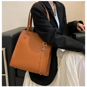 Minimalist caramel brown leather tote bag with long shoulder strap and metal buckle