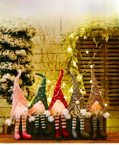 Close-up of five glowing knit Christmas gnomes with dangling striped legs on wooden base