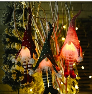 Three glowing Christmas gnomes with LED lights and sequin legs on winter branches