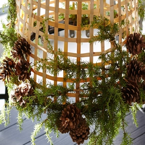 Close-up of a rustic woven wooden basket decorated with natural pine cones and green needles