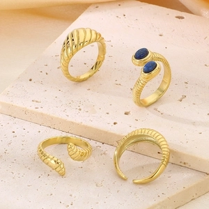 Golden snake-style stainless steel rings with blue gemstones on a beige stone base