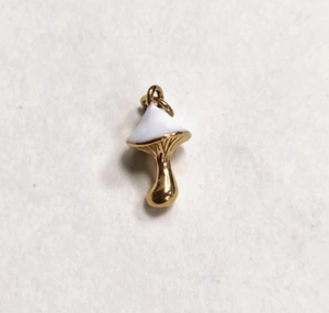 Macro shot of gold mushroom pendant with white enamel top and polished metallic finish