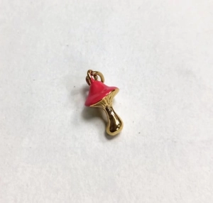 Macro shot of a red enamel mushroom pendant with a golden metal stem for DIY jewelry crafts