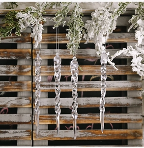 Close-up of four transparent spiral icicle ornaments hanging on snowy pine branches