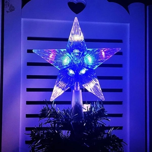 Macro shot of a transparent plastic star tree topper with blue LED light on a green branch